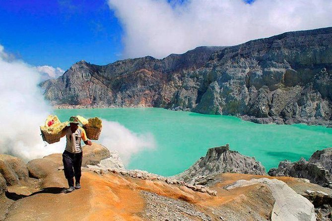 A miner carrying two loaded baskets along the path high above the crater lake