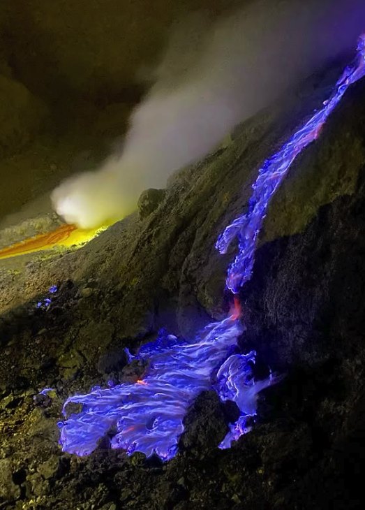 Blue flames burning over molten sulfur on the dark rock of the crater floor