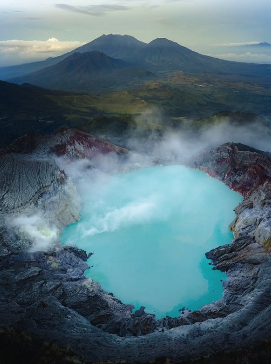 The full oval of the Ijen crater lake seen from above, with volcano peaks beyond
