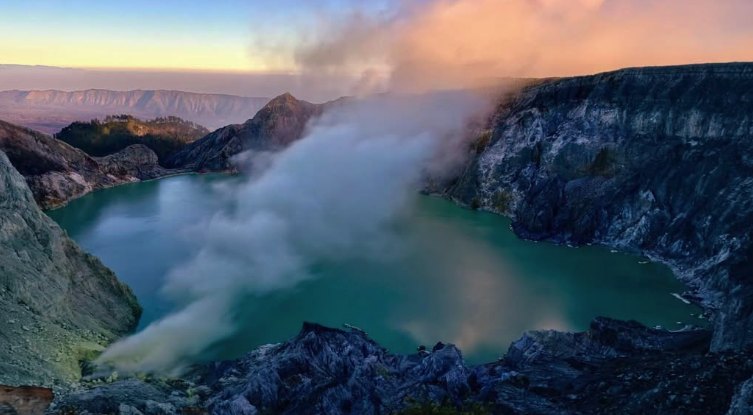 Steam drifting across the pale green crater lake below the rim wall of Kawah Ijen
