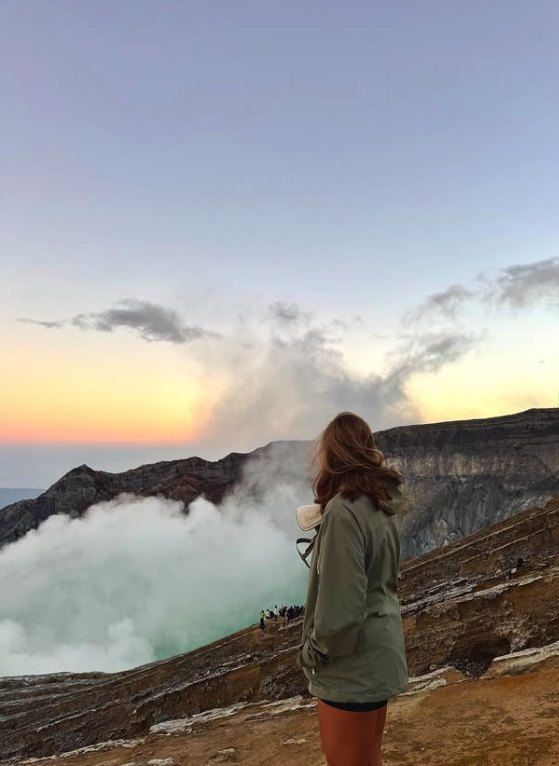 A walker at the rim looking down into the smoking crater as the sun comes up