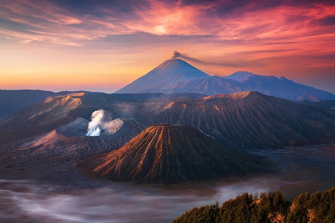 The cone of Mount Bromo smoking above the caldera floor under a red dawn sky