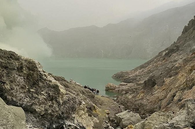 The grey rock wall of the crater dropping to the still surface of the acid lake