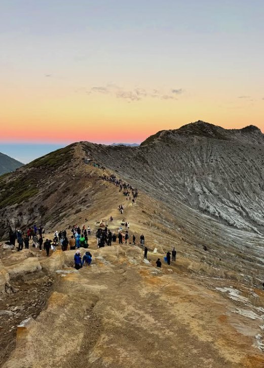 Walkers spread along the bare ridge of the crater rim with a coloured sunrise sky