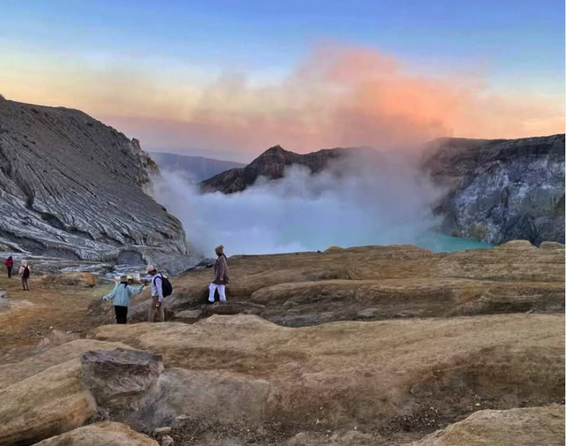 People standing on the flat rock of the crater rim as light reaches the lake below